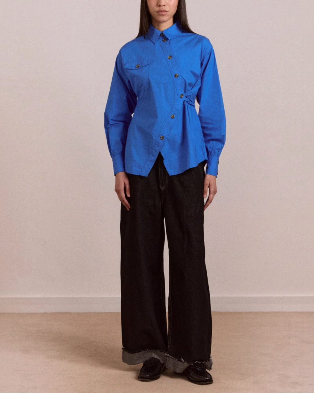 Modèle portant la chemise Lux bleue en coton biologique Merci Paris avec patte de boutonnage asymétrique