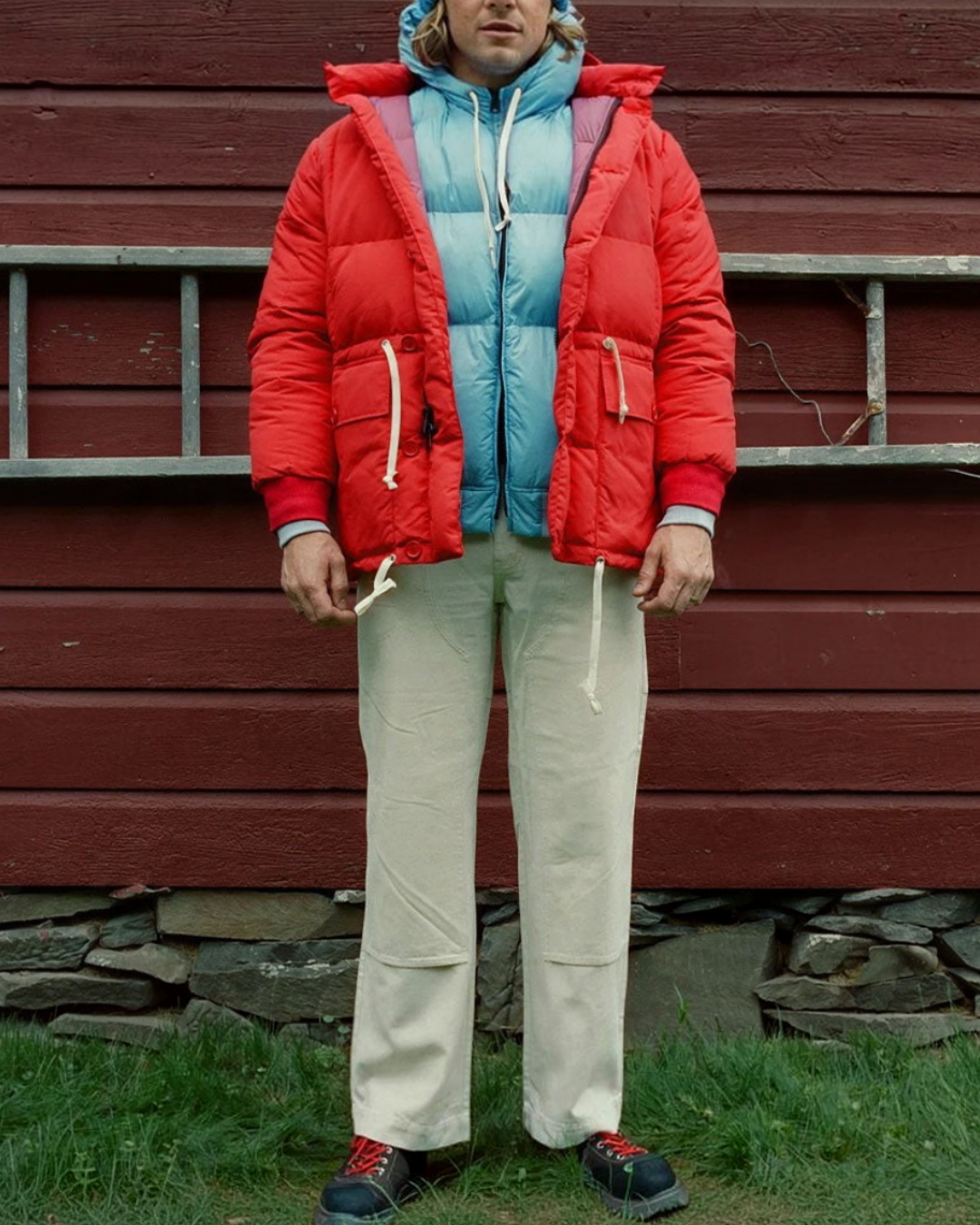 Homme portant une parka rouge Big Rock Candy avec doublure bleue, style alpiniste vintage, devant un mur en bois.