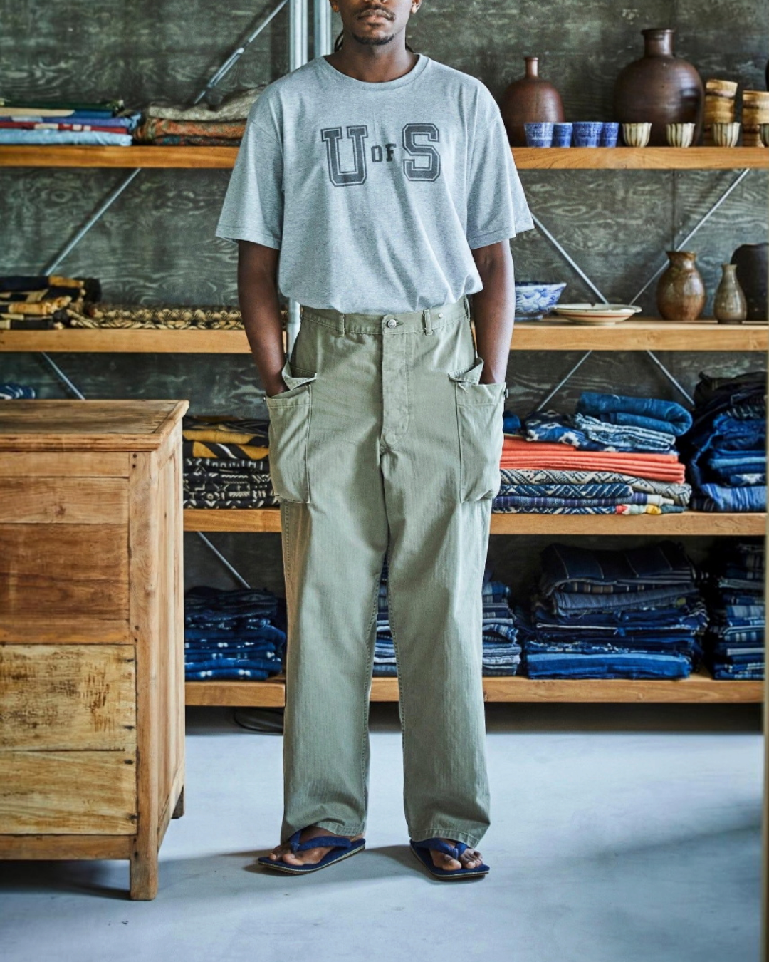 Homme portant un pantalon cargo kaki OrSlow en coton avec poches plaquées, présenté par Merci Paris dans une boutique