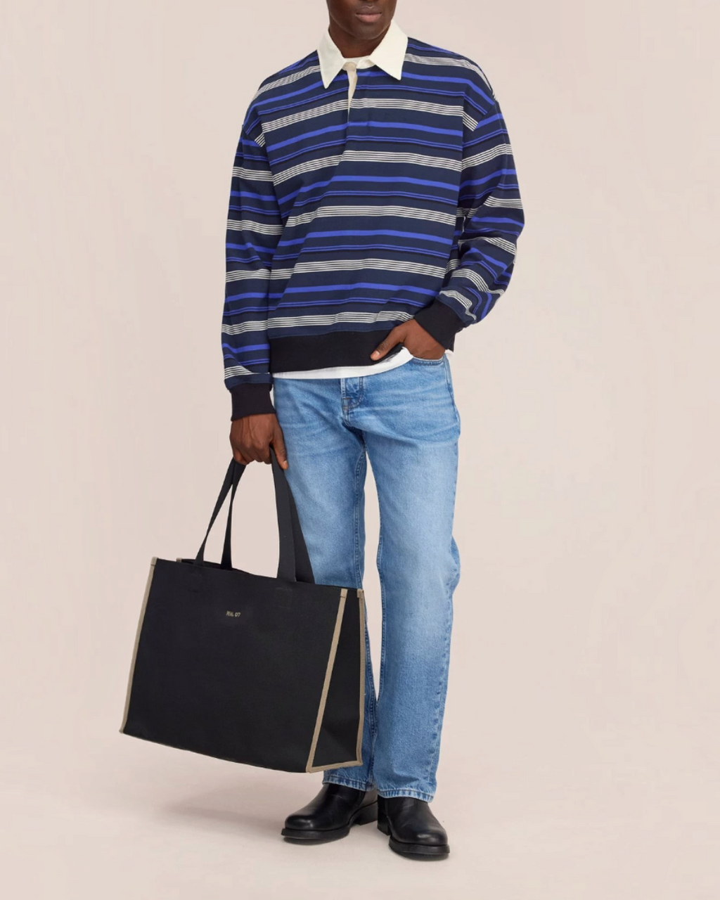 Homme portant le polo rayé bleu Merci Paris NN.07 à manches longues avec col contrastant et un grand sac fourre-tout