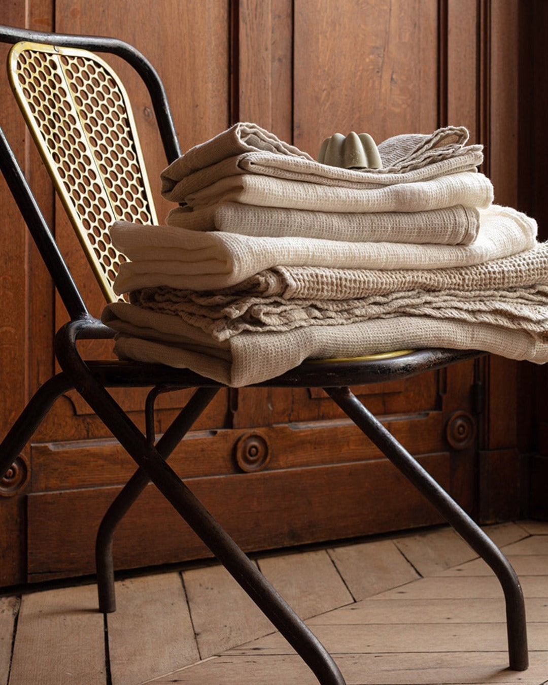 Serviettes de bain Merci Paris en lin nid d'abeille couleur pierre pliées sur une chaise en métal vintage