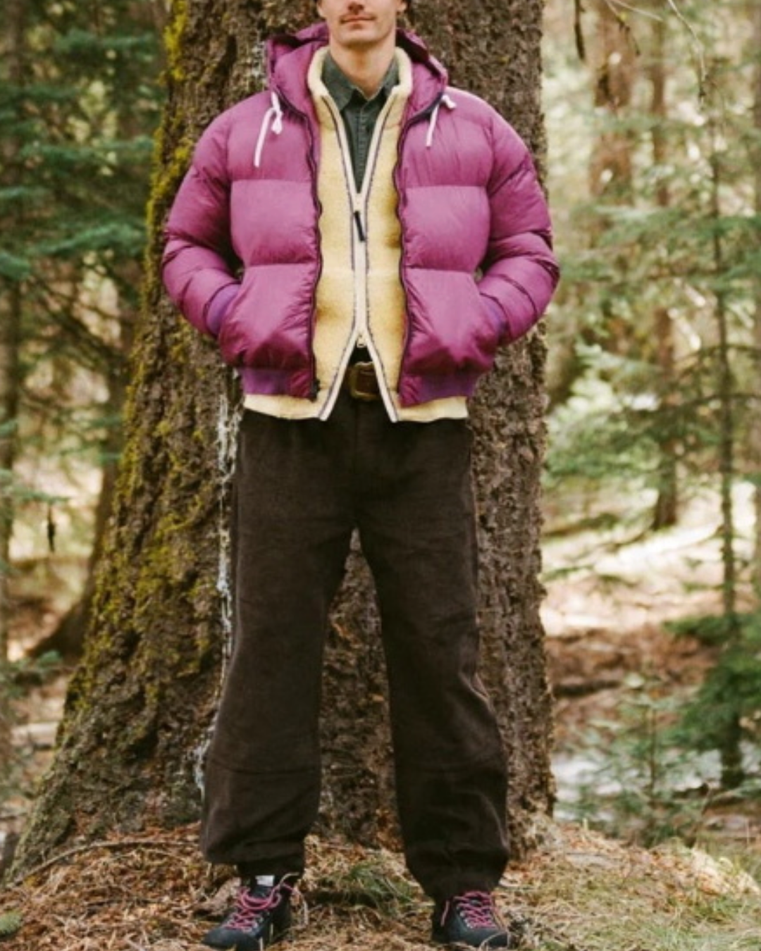Homme portant une doudoune Alpine Merci Paris Big Rock Candy couleur radicchio dans une forêt de conifères