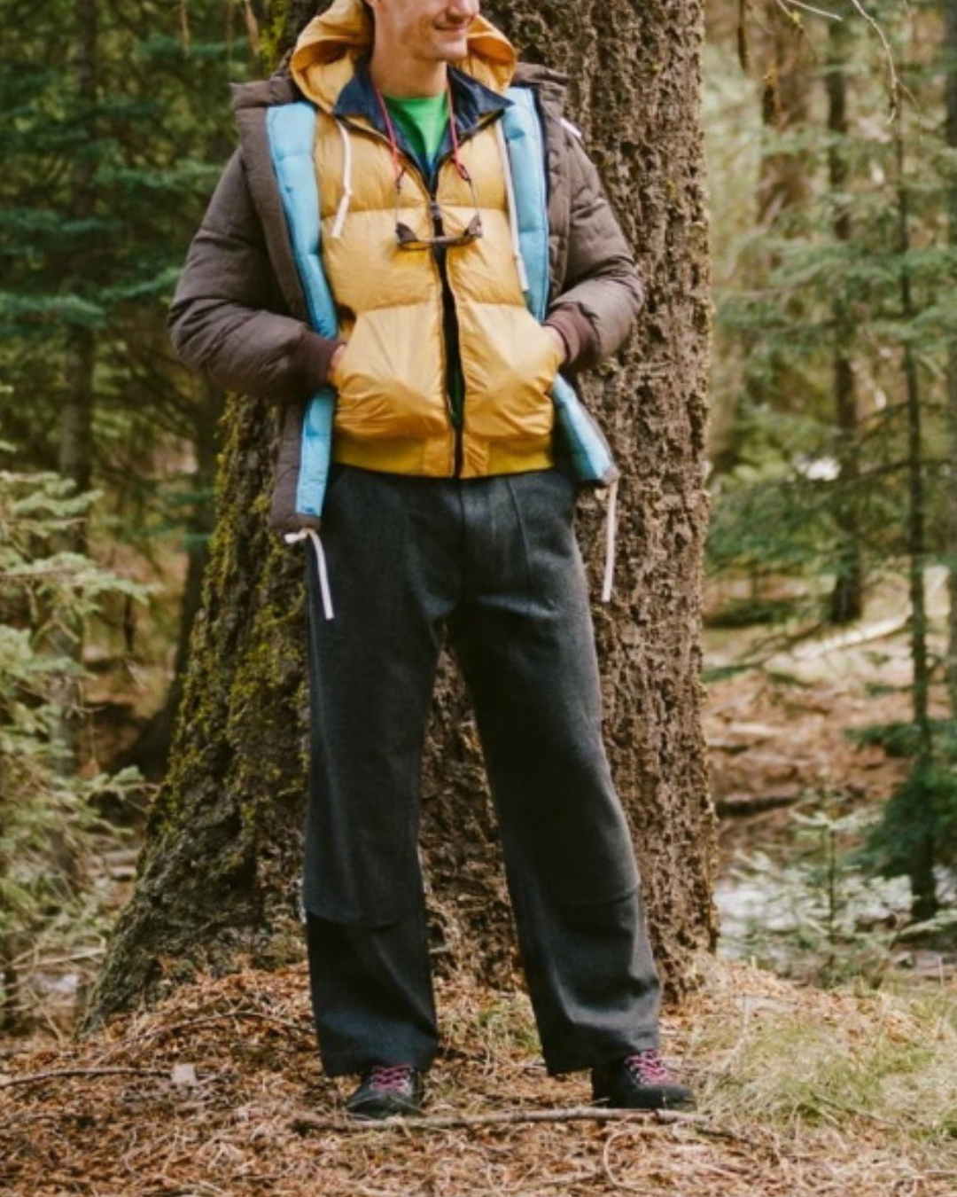 Homme portant la parka Arctic couleur cappuccino de Merci Paris dans une forêt, style alpiniste vintage matelassé.