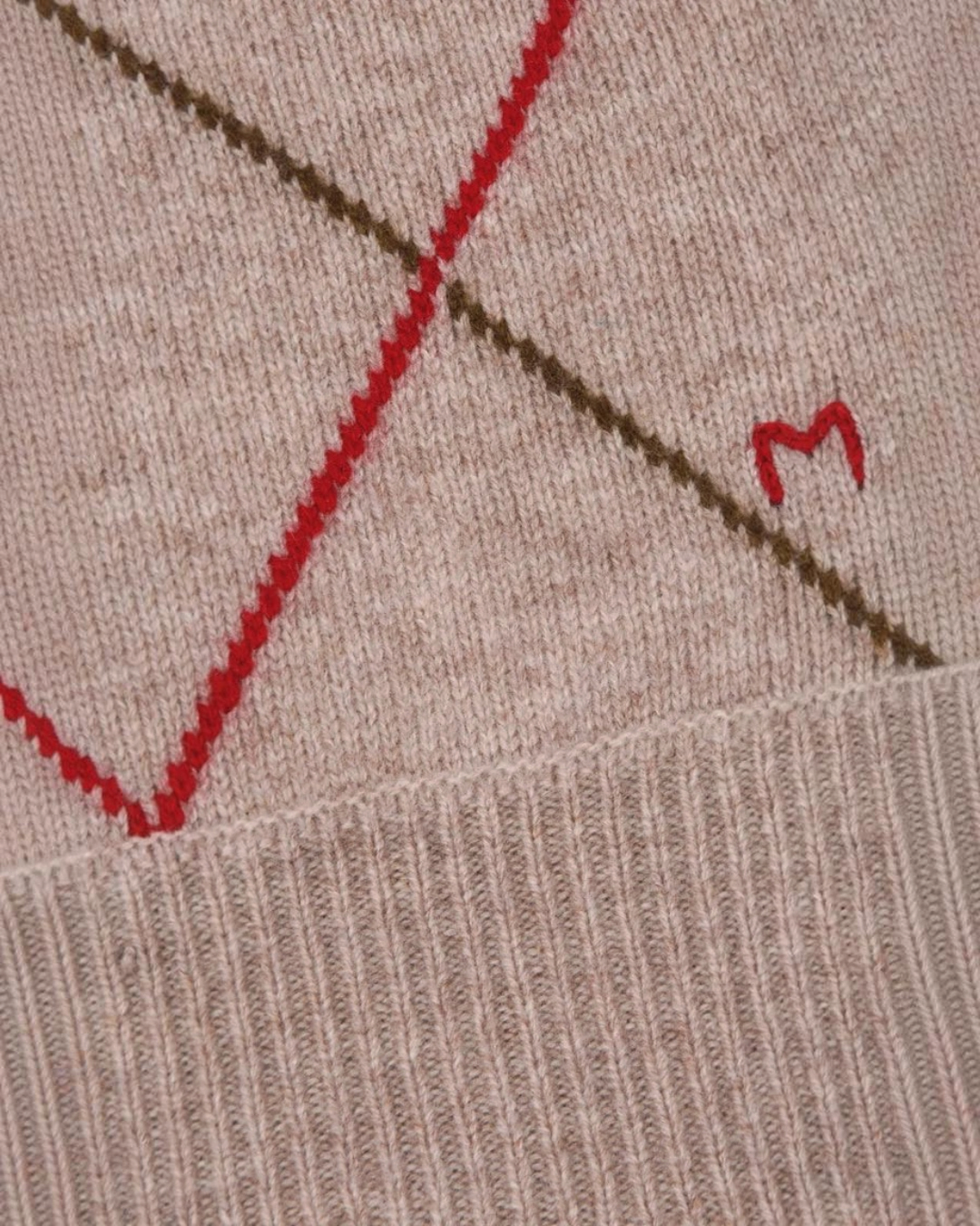 Gros plan sur le gilet Auguste Merci Paris en laine mérinos beige avec motif argyle rouge et broderie M