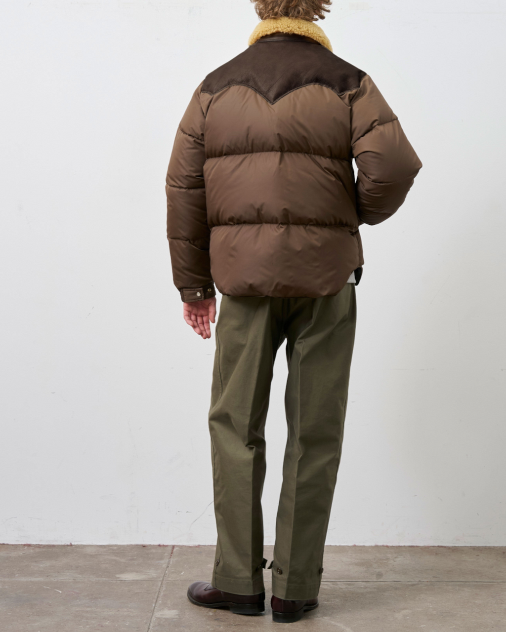 Homme portant une doudoune Merci Paris Rocky Mountain marron avec empiècement en cuir et col en peau lainée, vue dos