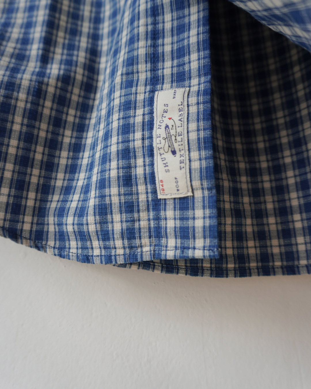 Gros plan sur le tissu en coton bleu indigo à carreaux de la chemise Merci Paris Dopple & Scent avec étiquette
