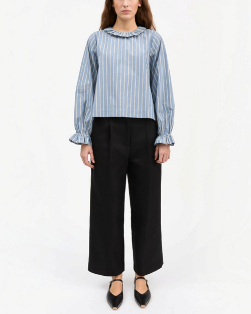 Modèle portant une blouse Skall Studio en coton biologique bleu à rayures, col rond volanté et manches bouffantes