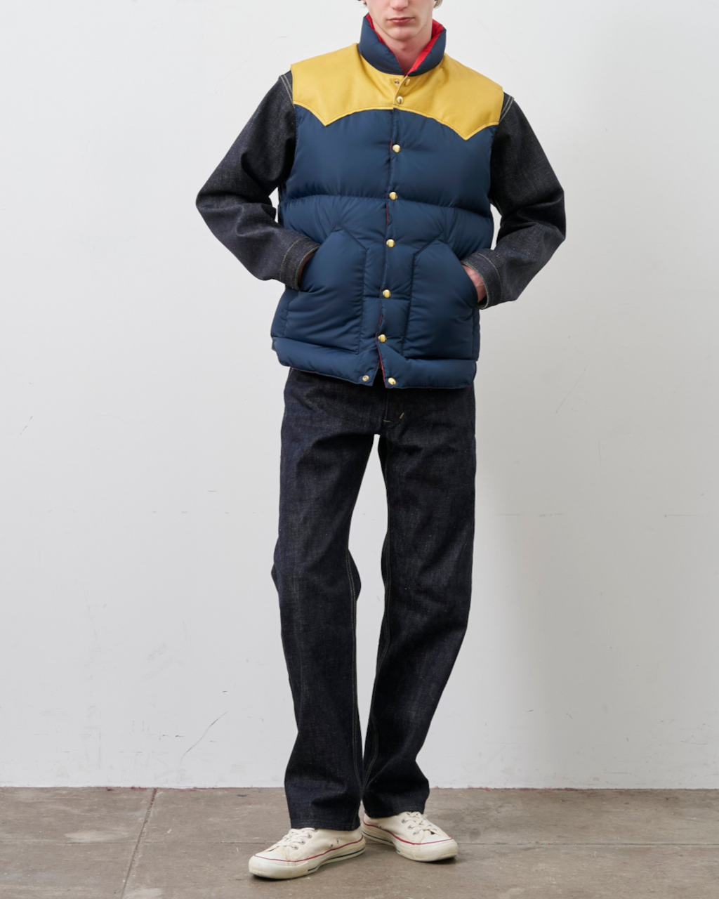 Homme portant un gilet en duvet Merci Paris Rocky Mountain bleu marine et jaune avec empiècement en cuir contrasté
