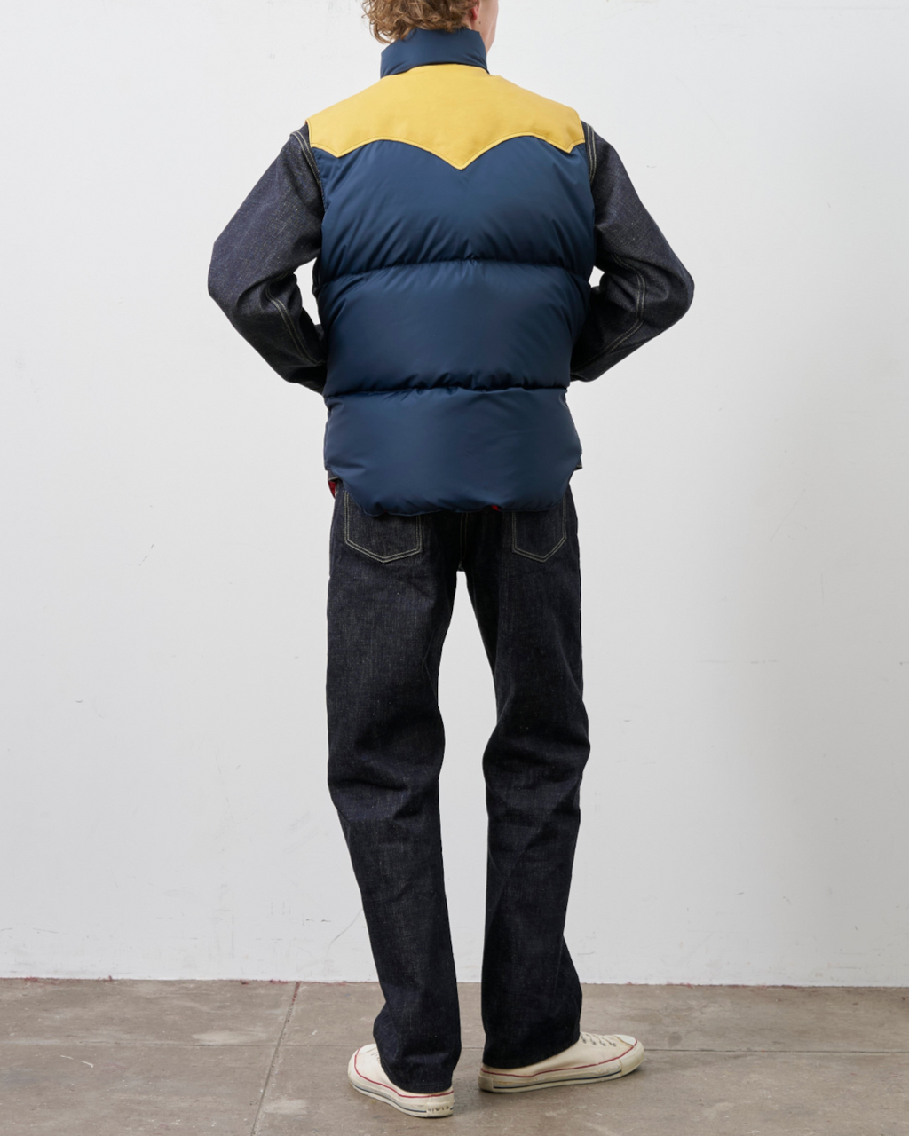 Homme portant un gilet en duvet Merci Paris Rocky Mountain bleu marine et jaune avec empiècement en cuir, vue dos