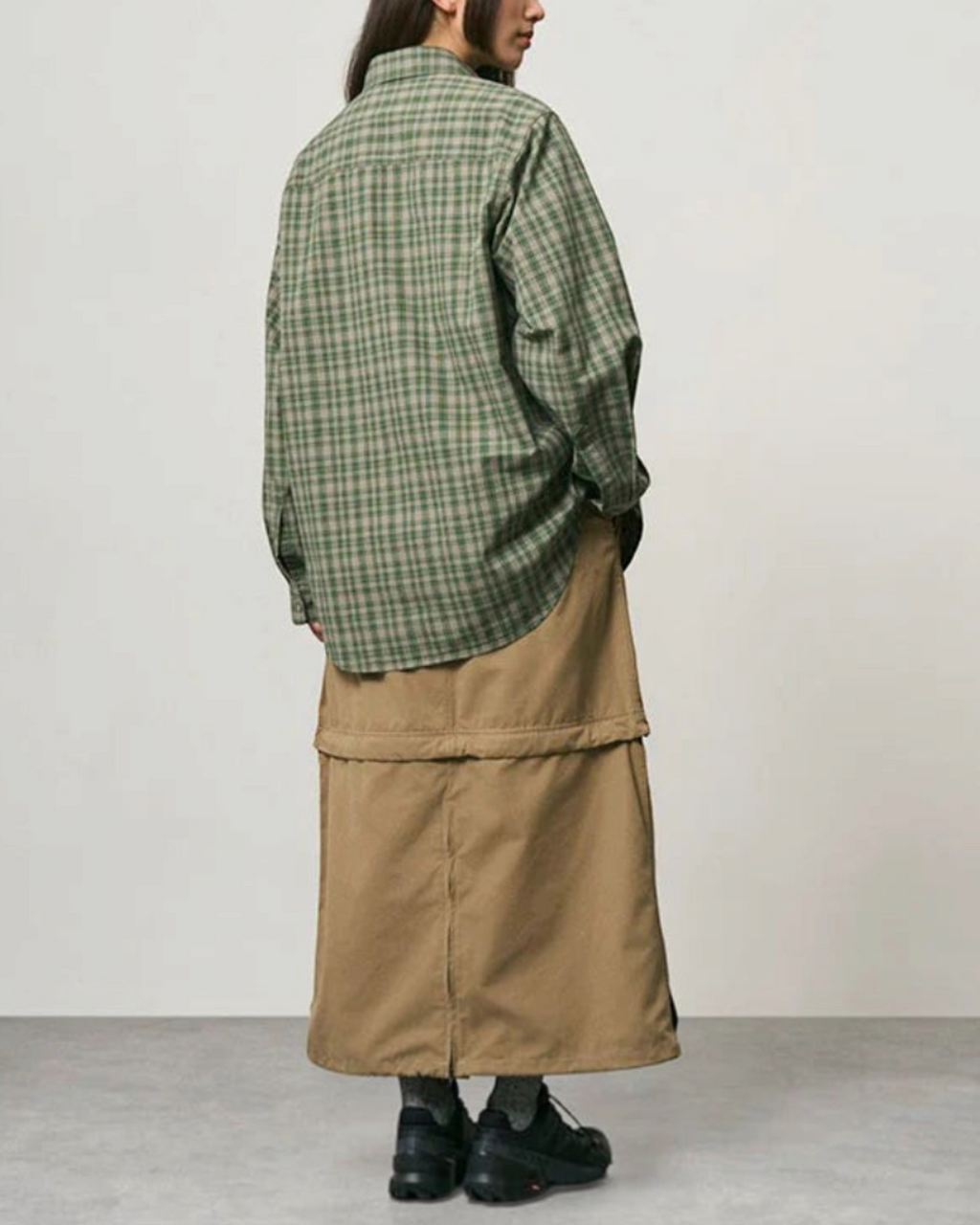Vue arrière d'une femme portant une chemise épaisse à carreaux verts Gramicci Merci Paris avec une jupe beige