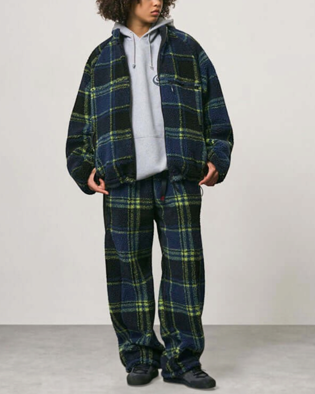 Modèle portant une veste réversible Merci Paris Gramicci en polaire sherpa épaisse à carreaux noirs et verts