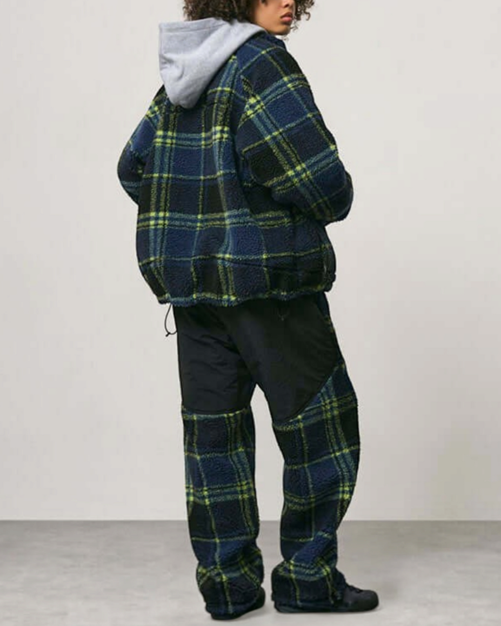 Modèle portant la veste réversible Merci Paris Gramicci en polaire sherpa à carreaux noirs et bleus sur sweat à capuche