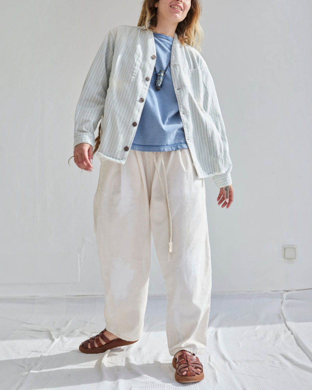 Modèle portant la veste Okinawa rayée bleu et écru de Merci Paris, coupe ample avec boutons en noix de coco.