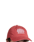 Casquette Merci Paris Bisous Skateboard en coton rouge brique délavé avec broderie blanche portée par un mannequin