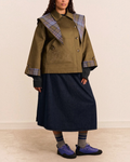 Modèle portant le trench court réversible Damson Madder couleur olive avec col à carreaux et broderie sur la poche