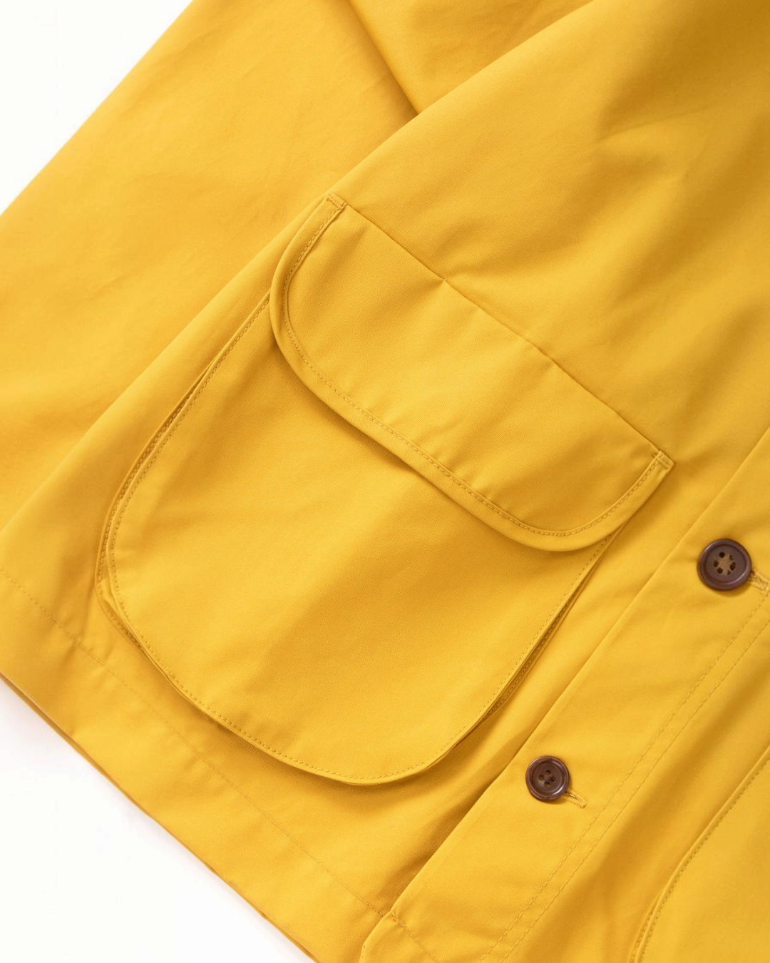 Gros plan sur la poche avant à soufflet d'une veste cirée jaune Merci Paris en coton biologique