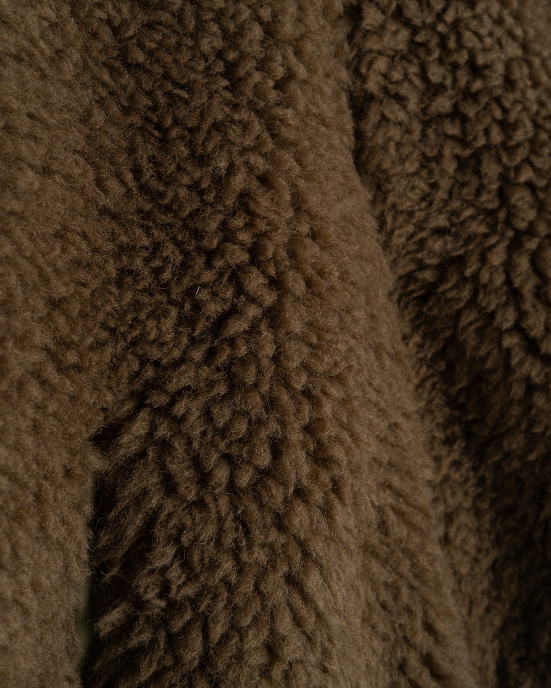 Gros plan sur la texture douce et duveteuse en fausse fourrure marron de la veste Alpine de Merci Paris