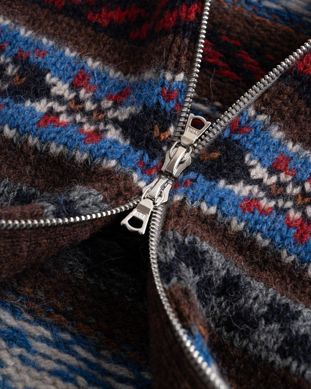 Gros plan sur la fermeture zippée en métal d'un cardigan Merci Paris Howlin' en laine Fair Isle multicolore