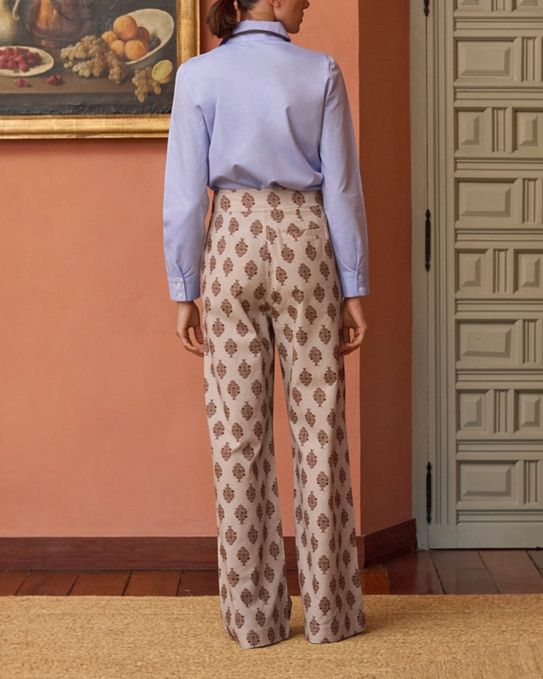 Vue arrière du pantalon Douglas beige à motifs de Merci Paris, porté avec une chemise bleue dans un intérieur élégant.