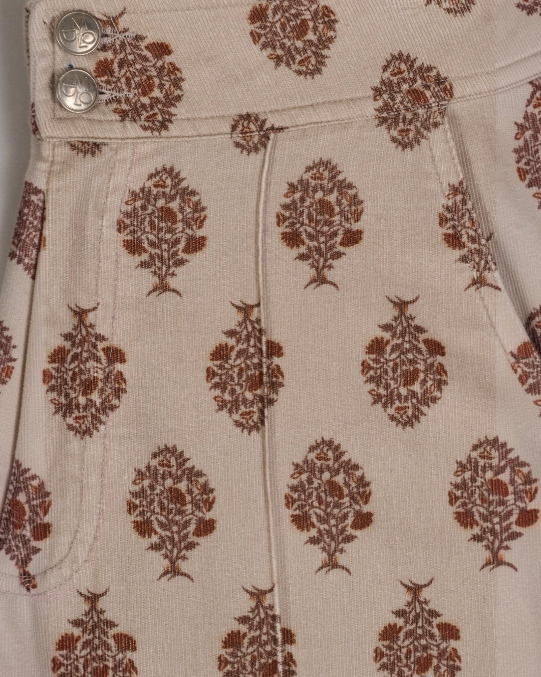 Gros plan sur le pantalon Douglas beige de Merci Paris avec un motif floral marron et des boutons métalliques gravés.