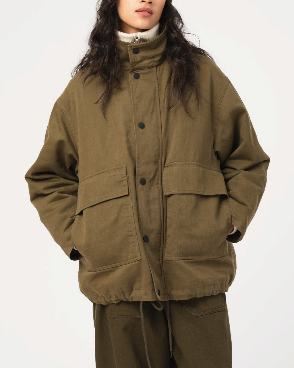 Modèle portant la veste Airborne en coton ciré Shitake de Merci Paris avec un bonnet marron et un col roulé blanc