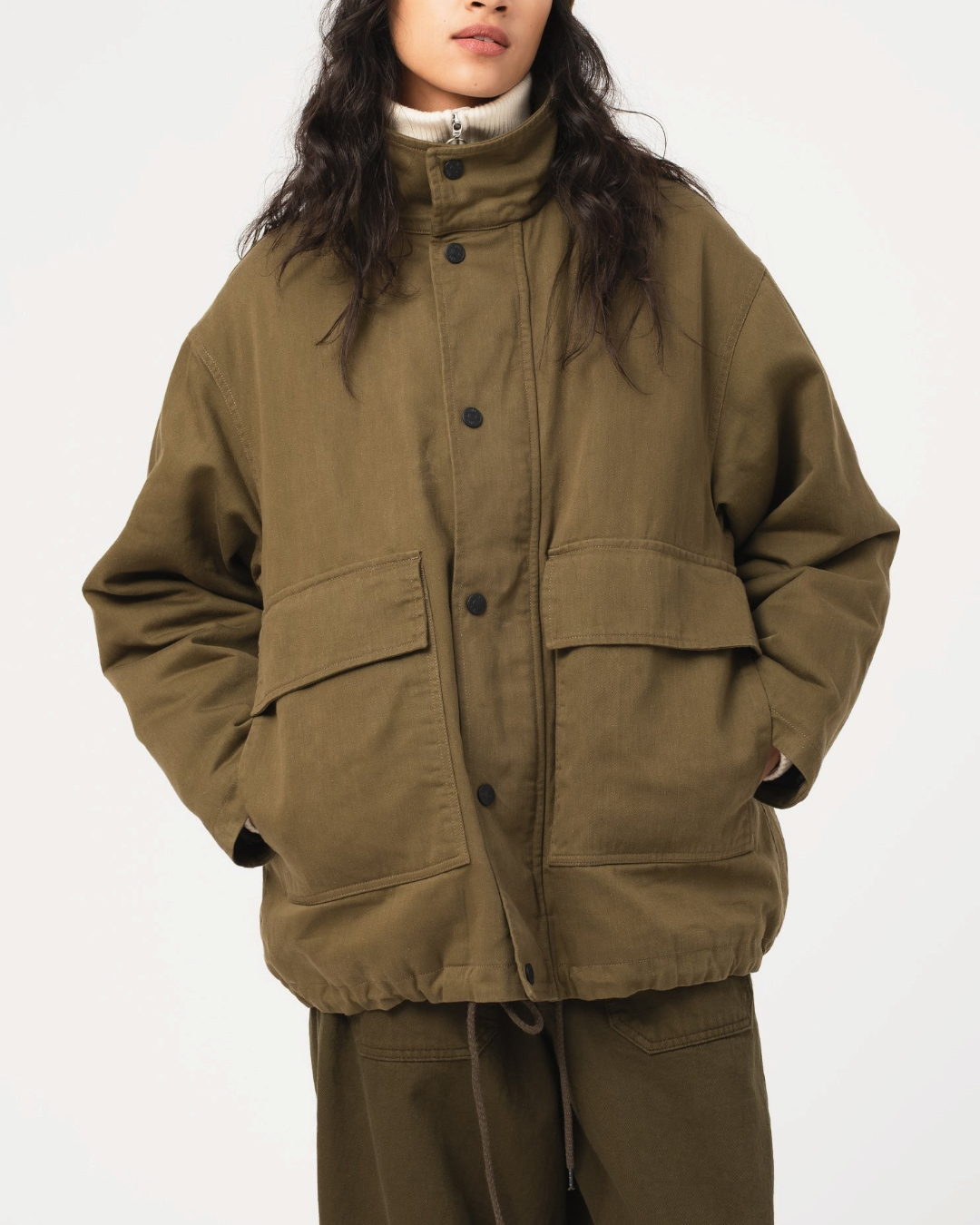 Modèle portant la veste Airborne en coton ciré Shitake de Merci Paris avec un bonnet marron et un col roulé blanc